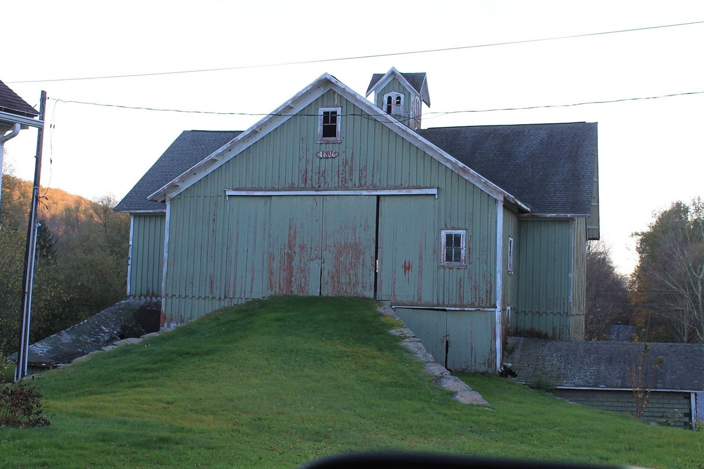 A historic green barn on a grassy hill
